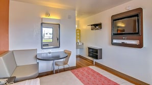 Habitación de hotel con una cama, un escritorio pequeño con una silla, un televisor montado en la pared y una ventana con vistas al exterior.