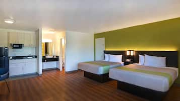 A hotel room with two beds, a kitchenette, and a bathroom.