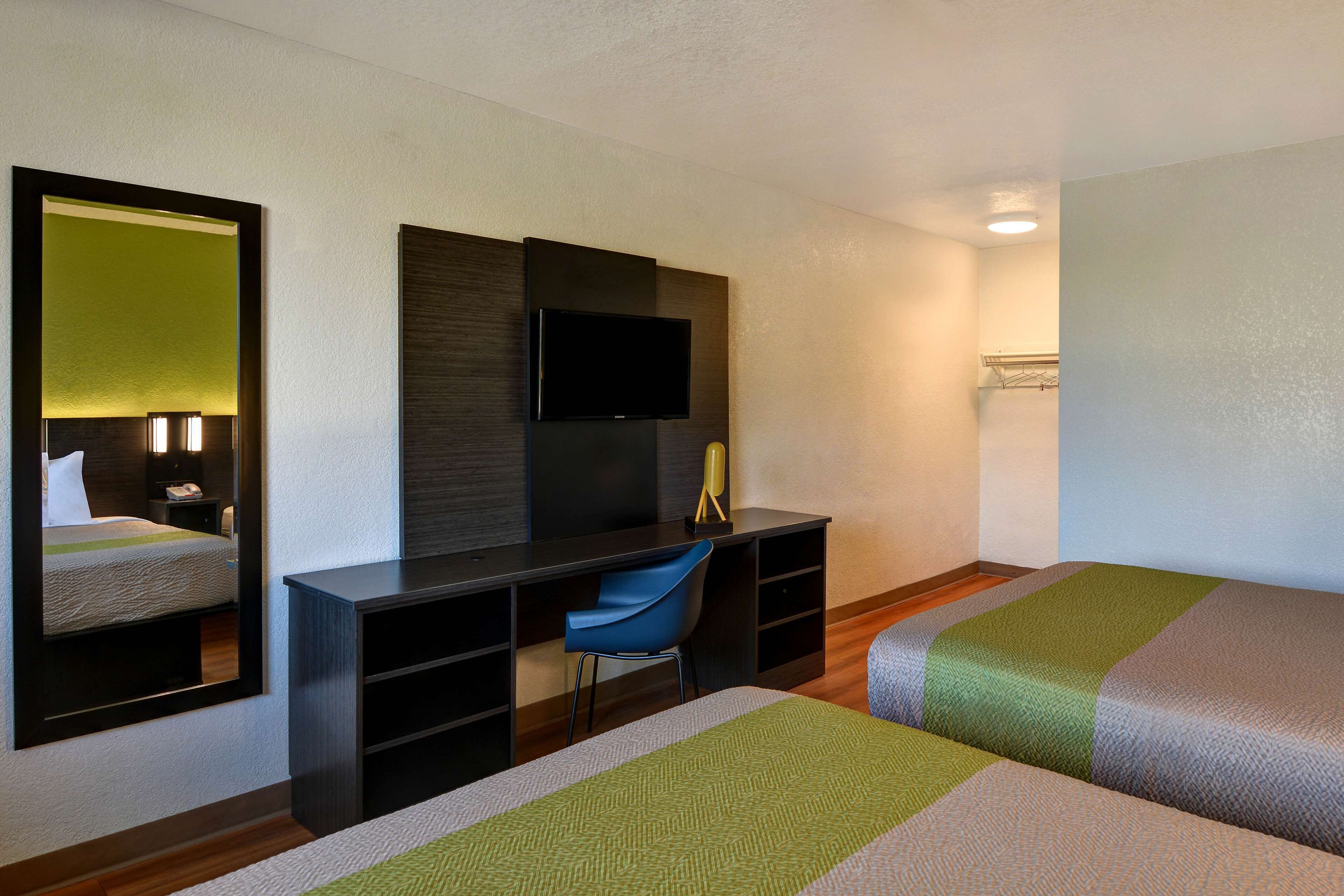 Una habitación de hotel con cama, escritorio, silla, televisor y espejo.