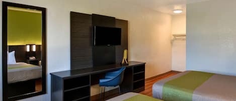 Una habitación de hotel con cama, escritorio, silla, televisor y espejo.