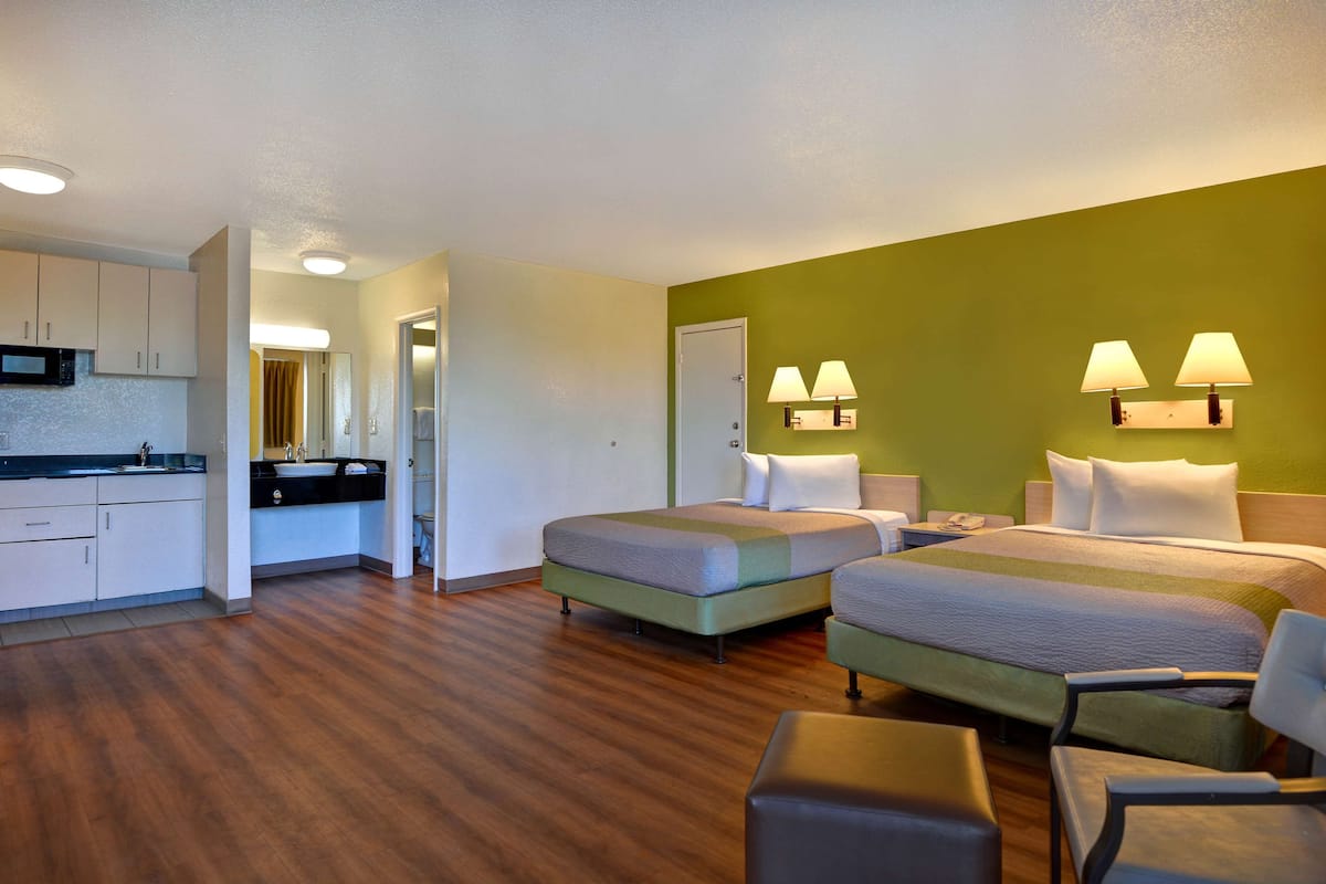 A hotel room with two beds, a kitchenette, and a bathroom.