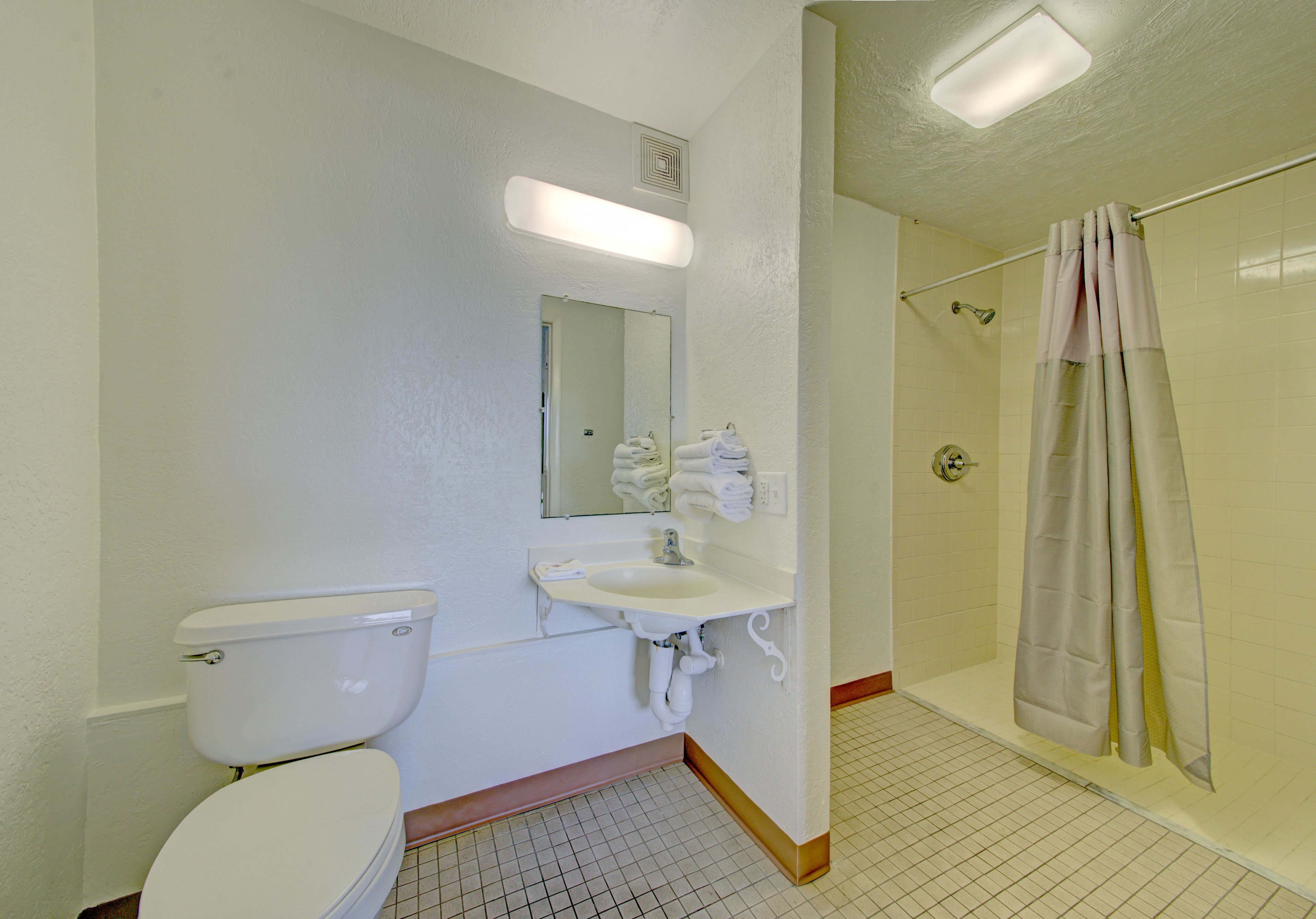 A bathroom with a toilet, sink, mirror, and shower.