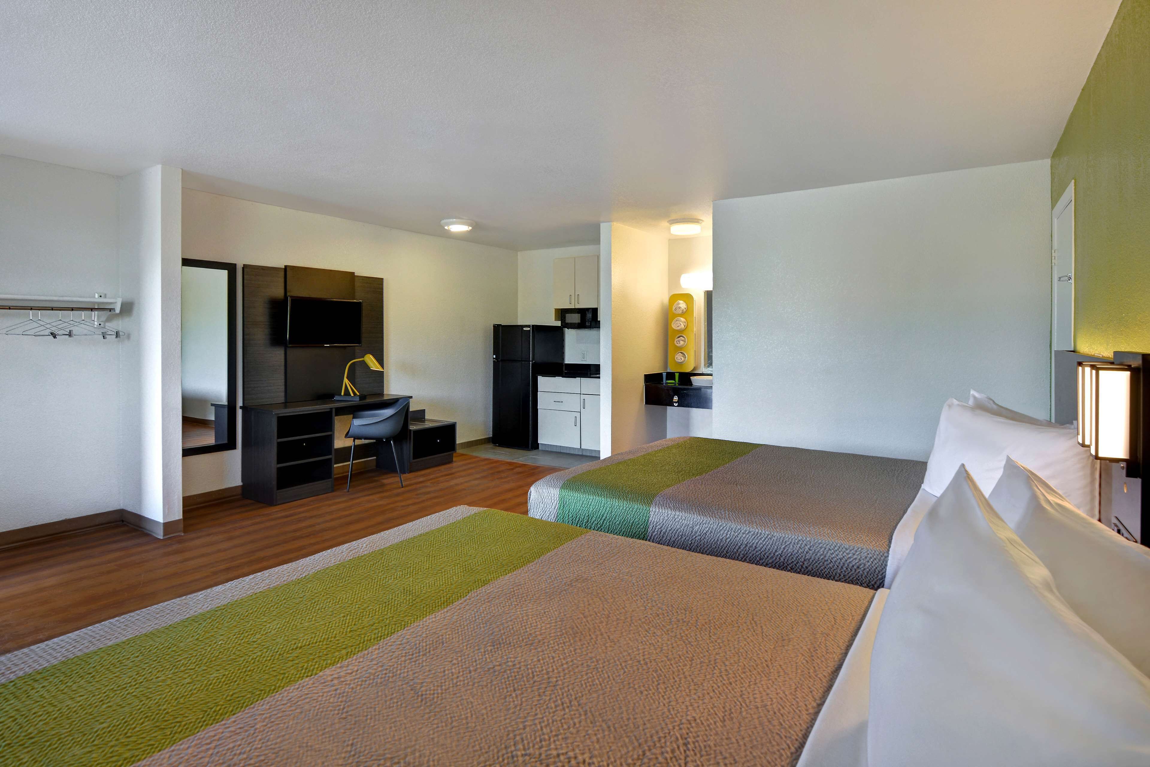 A hotel room with two beds, a desk, a chair, a TV, and a kitchenette.