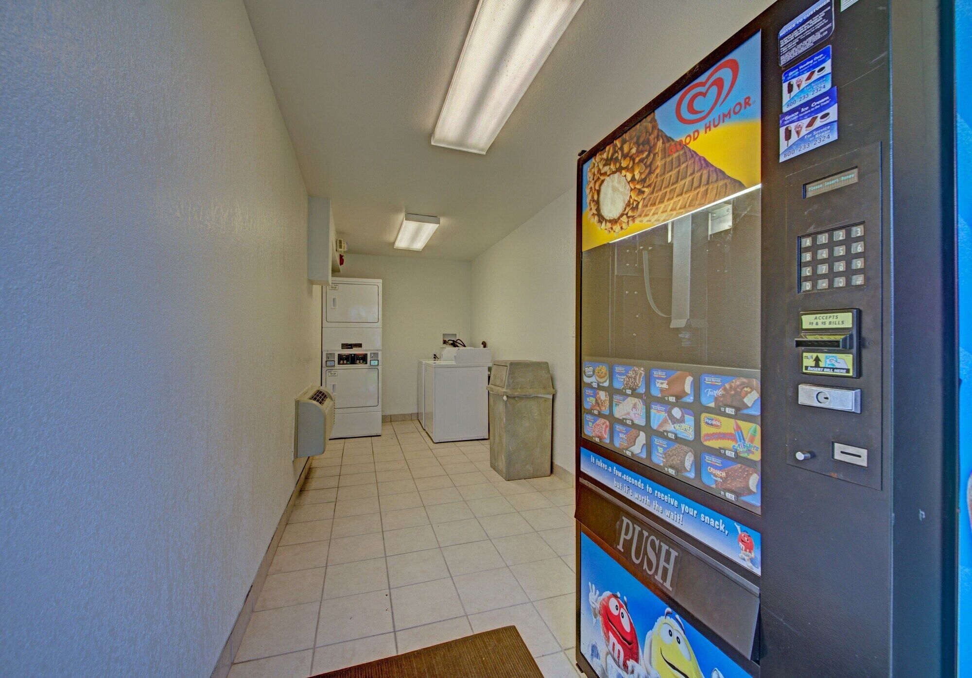 A hallway with a vending machine, a trash bin, and a small kitchenette area.