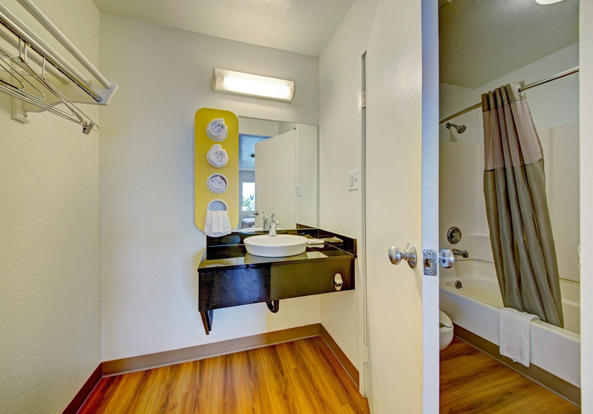 A bathroom with a wooden floor, a sink with a black countertop, a mirror, and a shower with a curtain.