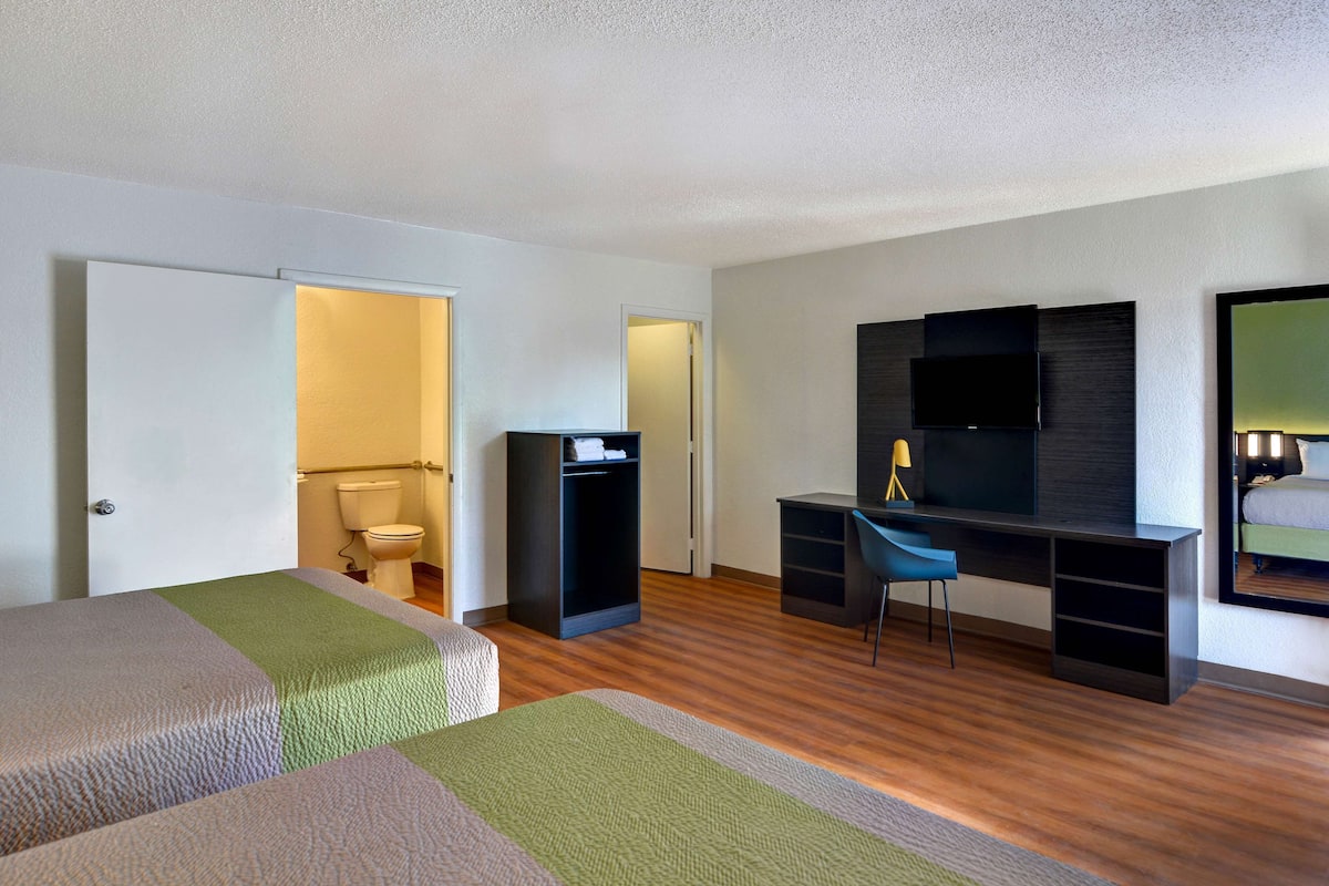 A hotel room with two beds, a desk, a chair, a TV, and a mirror.