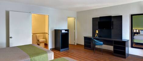 Ein Hotelzimmer mit zwei Betten, einem Schreibtisch, einem Stuhl, einem Fernseher und einem Spiegel.