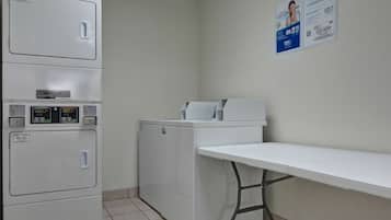 Un área de lavandería con lavadoras y secadoras apiladas, una mesa y un cartel en la pared.