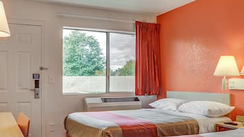 A hotel room with two beds, a window with curtains, a desk, and a lamp.