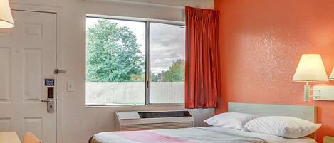 A hotel room with two beds, a window with curtains, a desk, and a lamp.