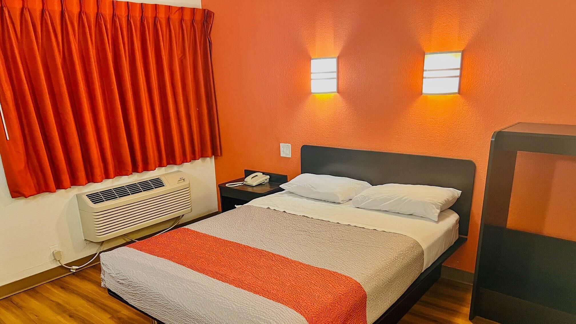 Ein Hotelzimmer mit einem Bett, einem Nachttisch, einem Telefon, einer Klimaanlage und zwei Wandleuchten.