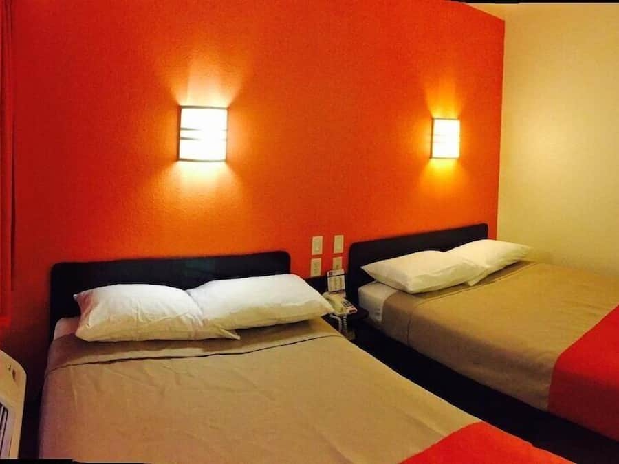 Quarto de hotel com duas camas, cortinas vermelhas e luminárias fixadas na parede.