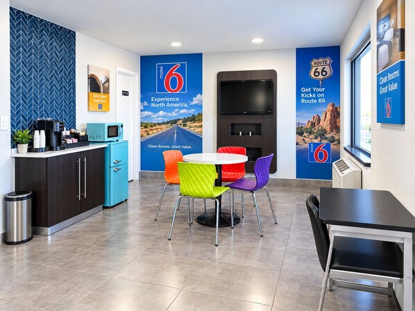 A modern hotel room with a kitchenette, a round table with colorful chairs, a flat-screen TV, and Route 66-themed decor. - Motel 6 Amarillo, TX - West (Amarillo)