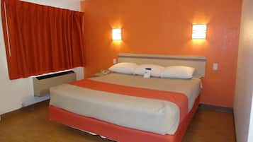 A hotel room with a bed, two bedside lamps, a window with curtains, and a wall-mounted heater.