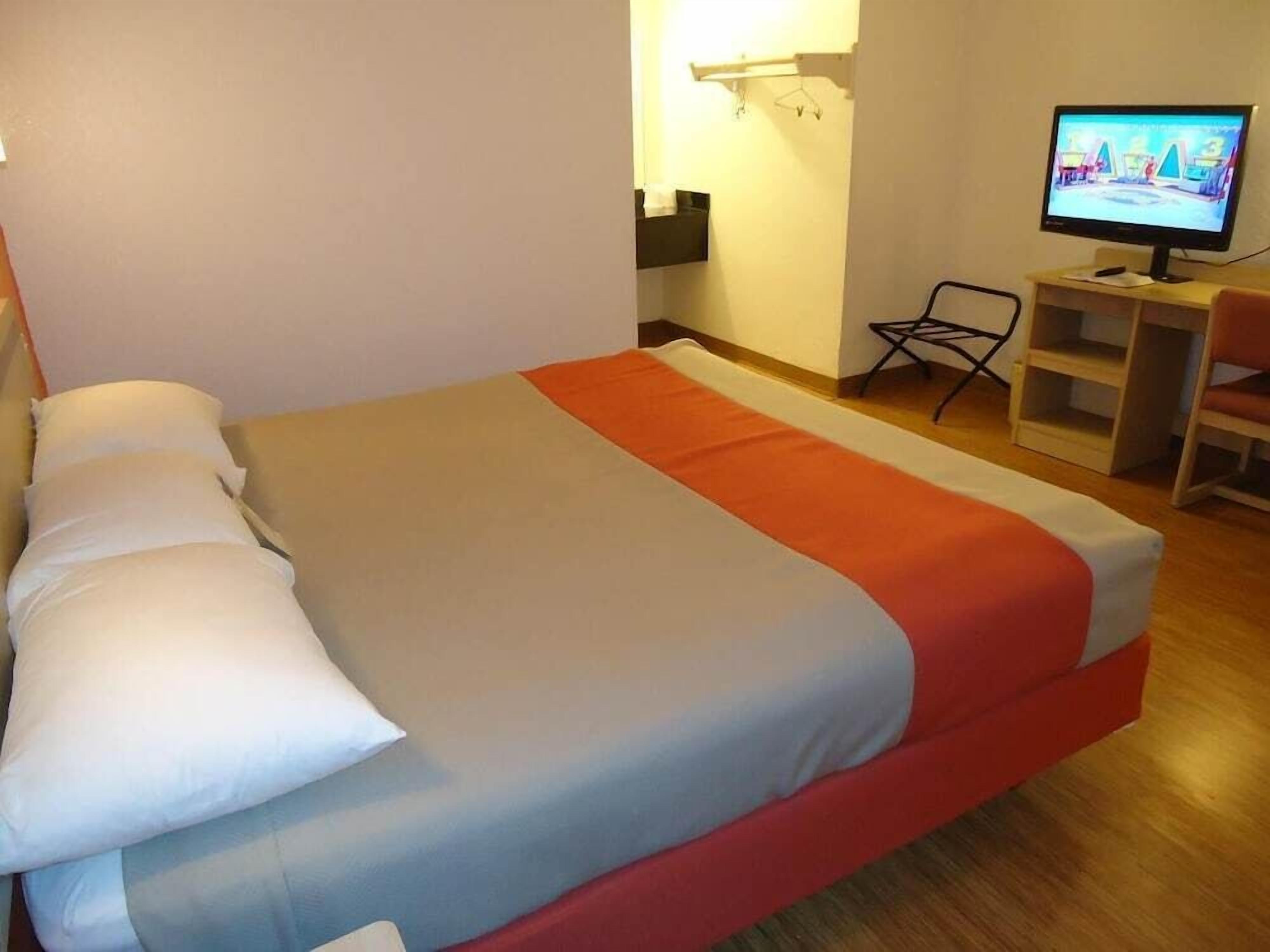 Una habitación de hotel con una cama, un televisor y un escritorio con una silla.