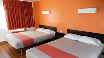 A hotel room with two beds, orange walls, and a window with red curtains.