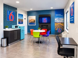 A modern motel room with a kitchenette, a dining area with colorful chairs, a TV, and a mural of a road. - Motel 6 Amarillo, TX - West (Amarillo)