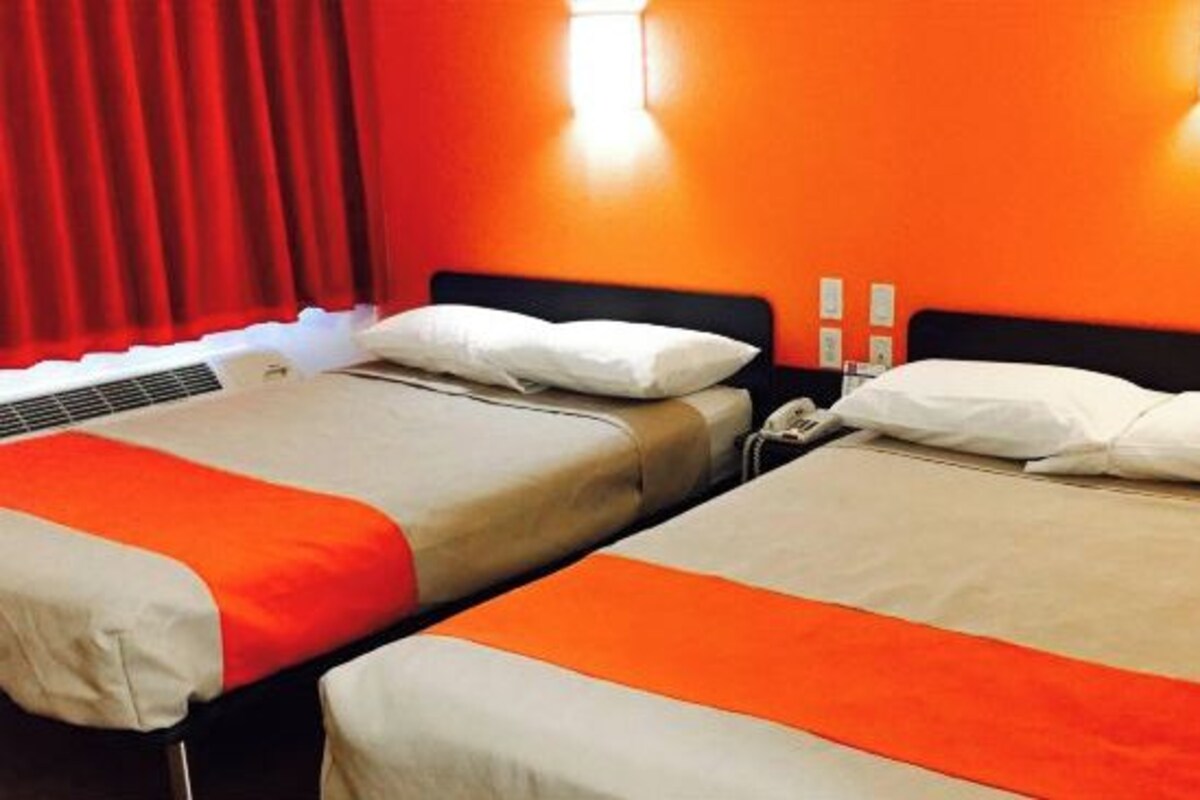 Une chambre d’hôtel avec deux lits, chacun équipé de draps blancs et orange, d’un radiateur et d’un téléphone.