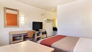 A hotel room with a desk, a television, a bed, and a mirror.