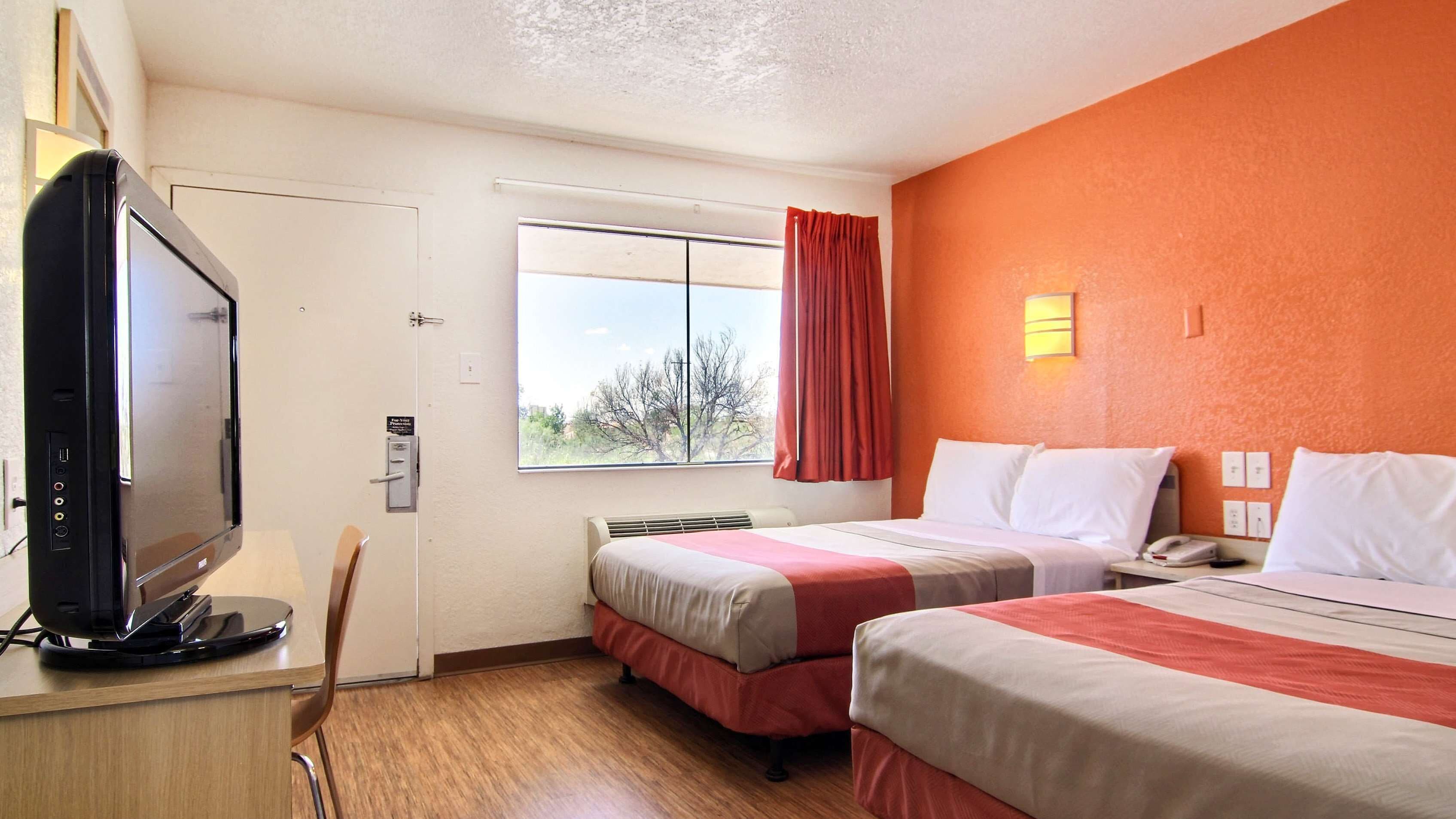 A hotel room with two beds, a television, a window with a view, and a red curtain.