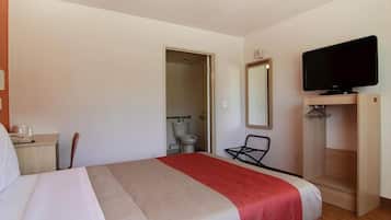 A hotel room with a bed, a television, a mirror, and a bathroom visible through an open door.