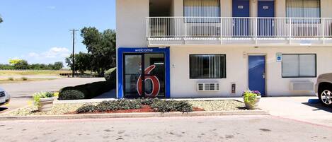 A two-story motel with a blue entrance door marked 'welcome' and numbered rooms 201 and 202.