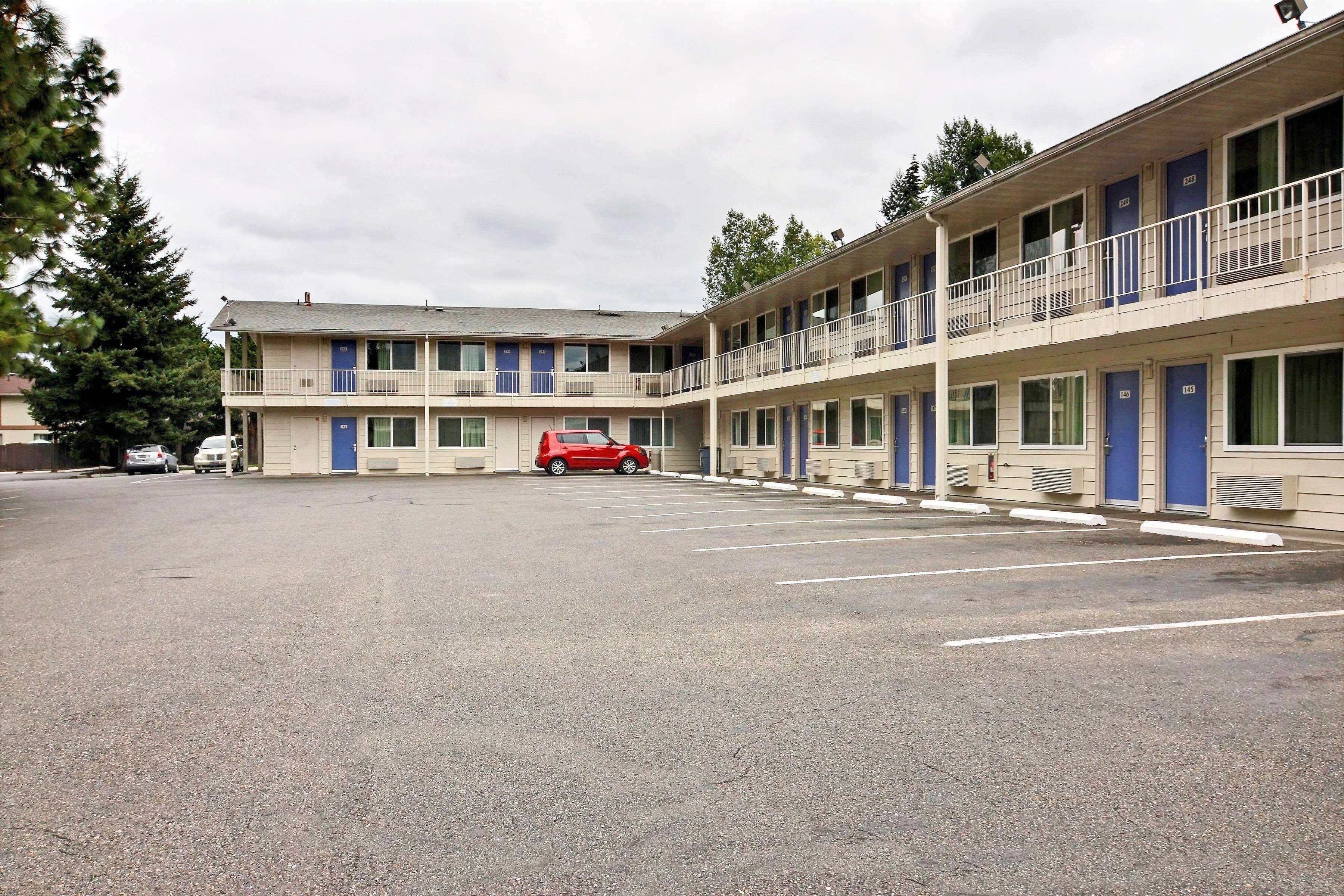 Un motel de varios pisos, un estacionamiento y un coche rojo aparcado allí.