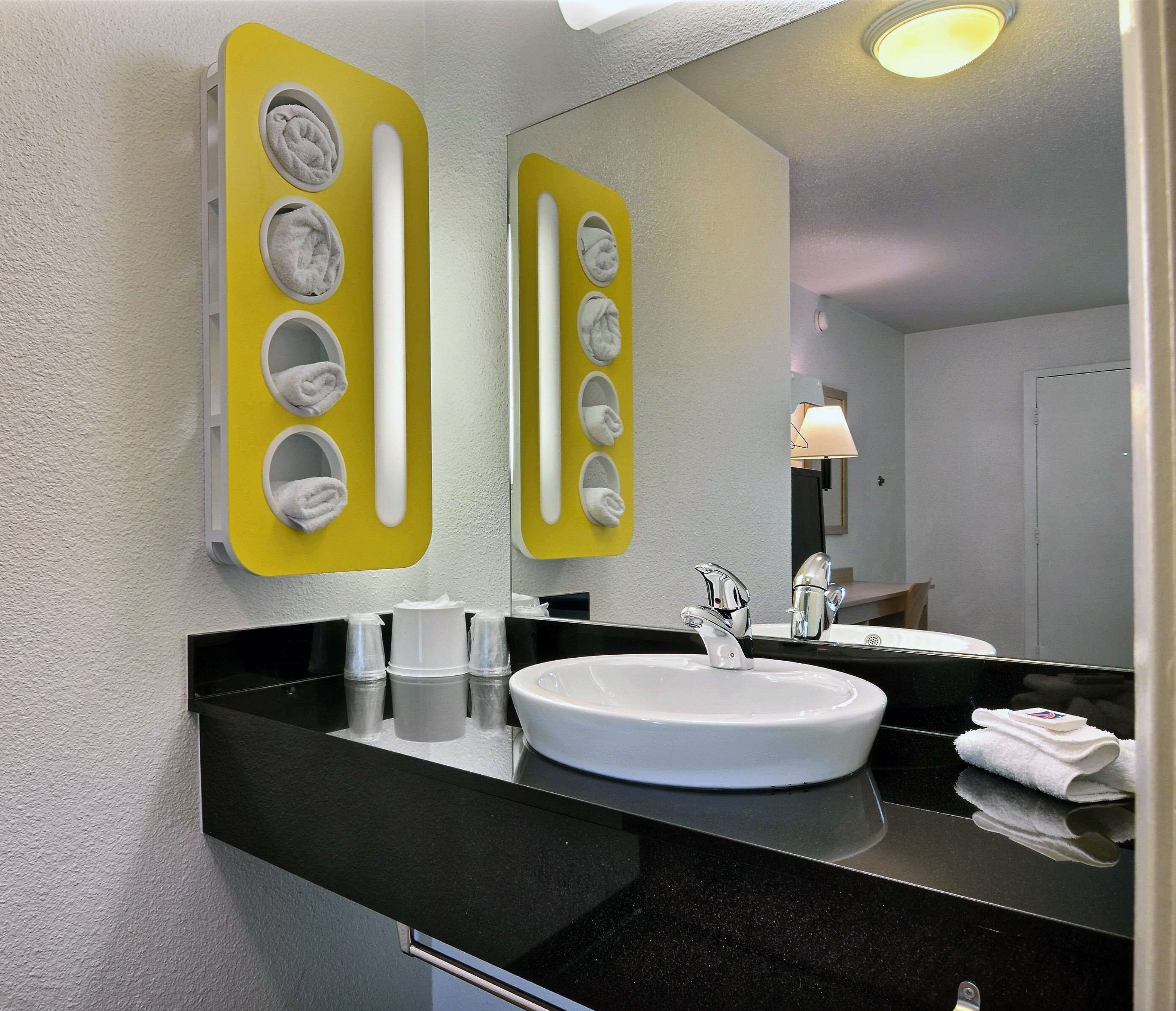 Um banheiro moderno com um espelho grande, uma pia branca e um porta-toalhas amarelo.