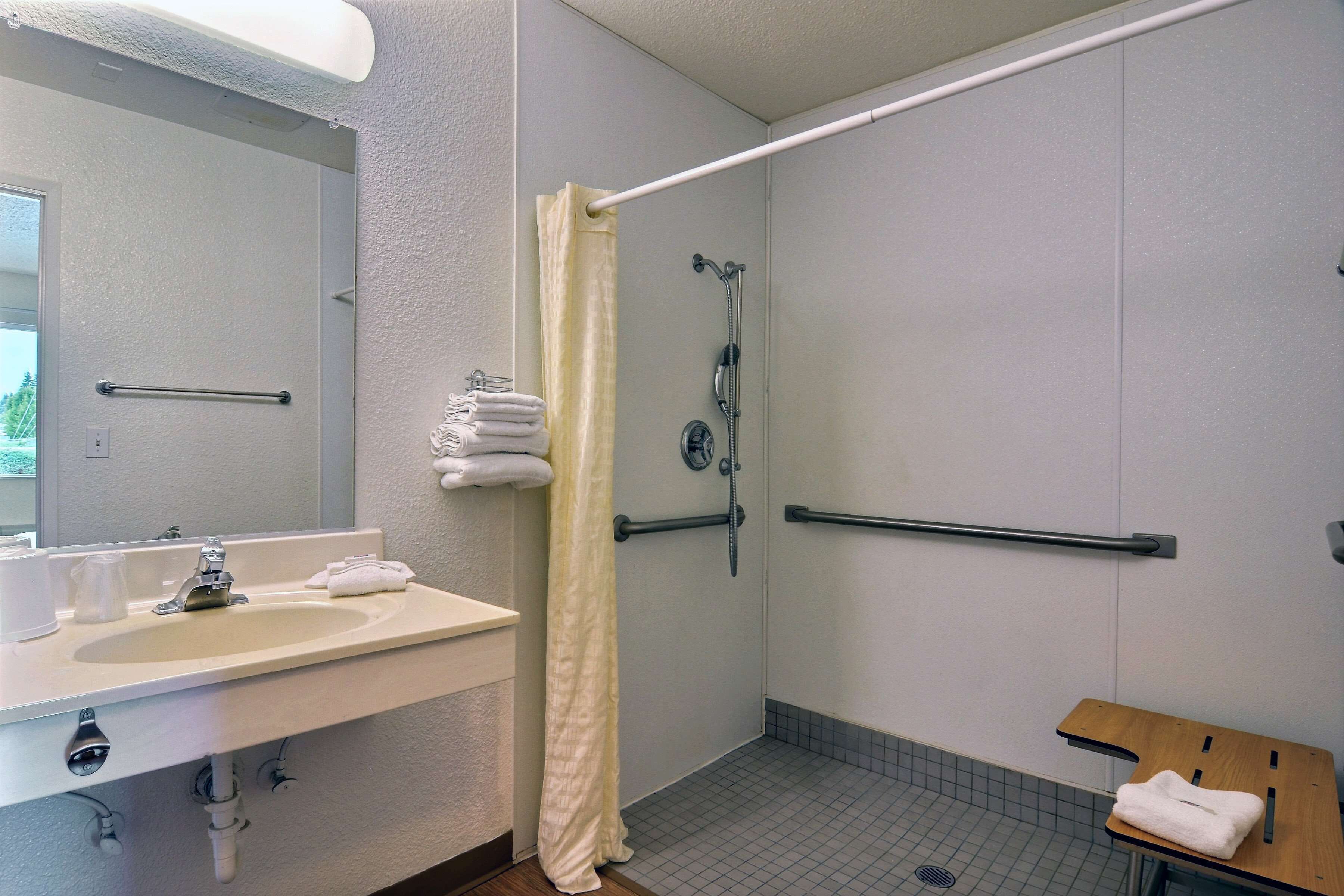 Un baño con lavamanos, espejo, ducha y barras de apoyo.