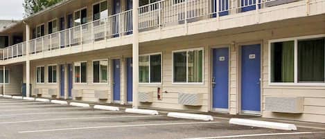 Un motel con varias habitaciones, cada una con puerta y ventana, y un estacionamiento al frente.