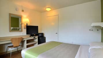A hotel room with a bed, a desk with a chair, a television, a microwave, and a door.