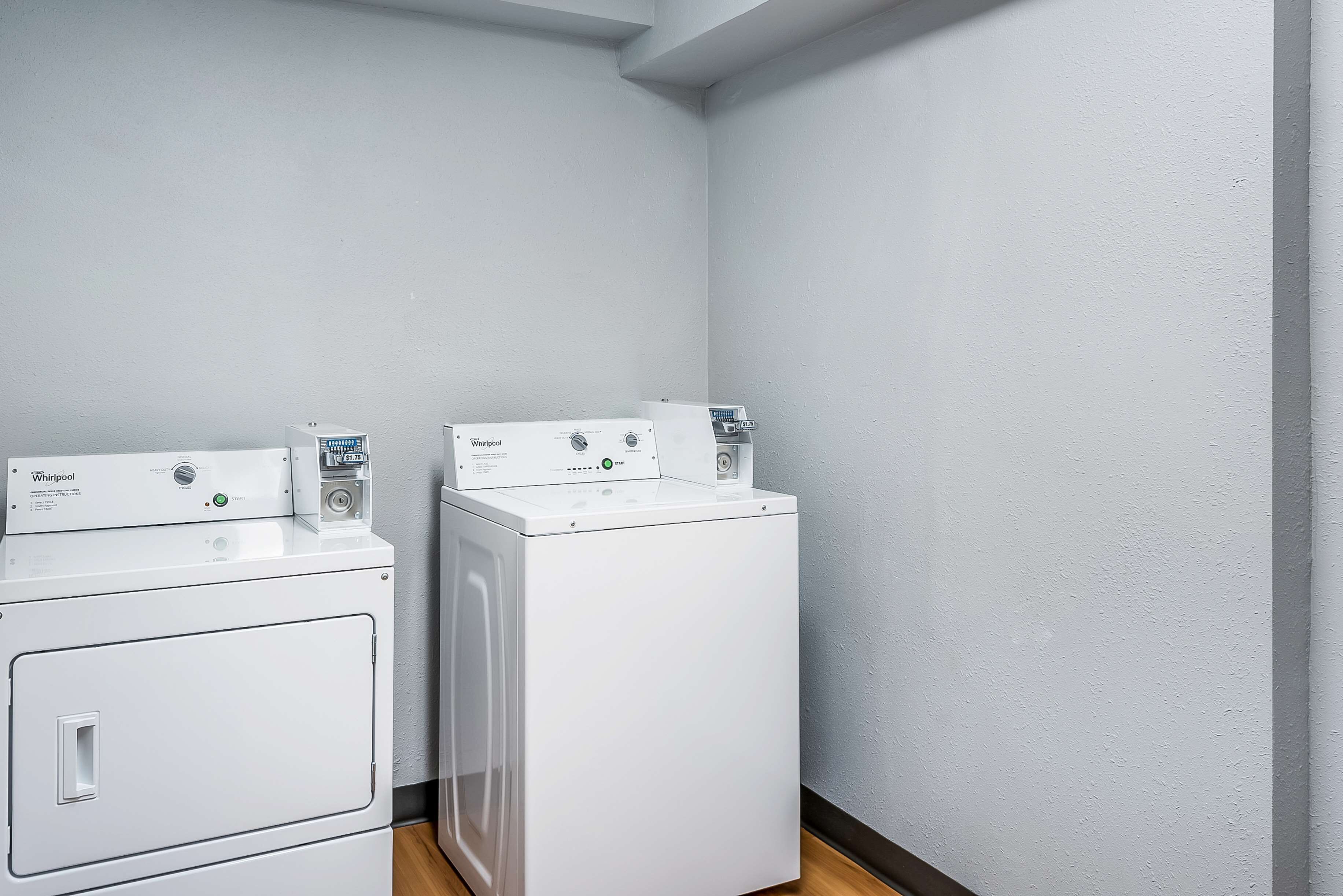 Pesuhuoneessa on kaksi valkoista Whirlpool-merkkiä olevaa, edestä täytettävää pyykinpesukonetta ja valkoinen kuivausrumpu.