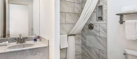 Un baño con lavamanos, espejo, ducha con cortina y retrete.