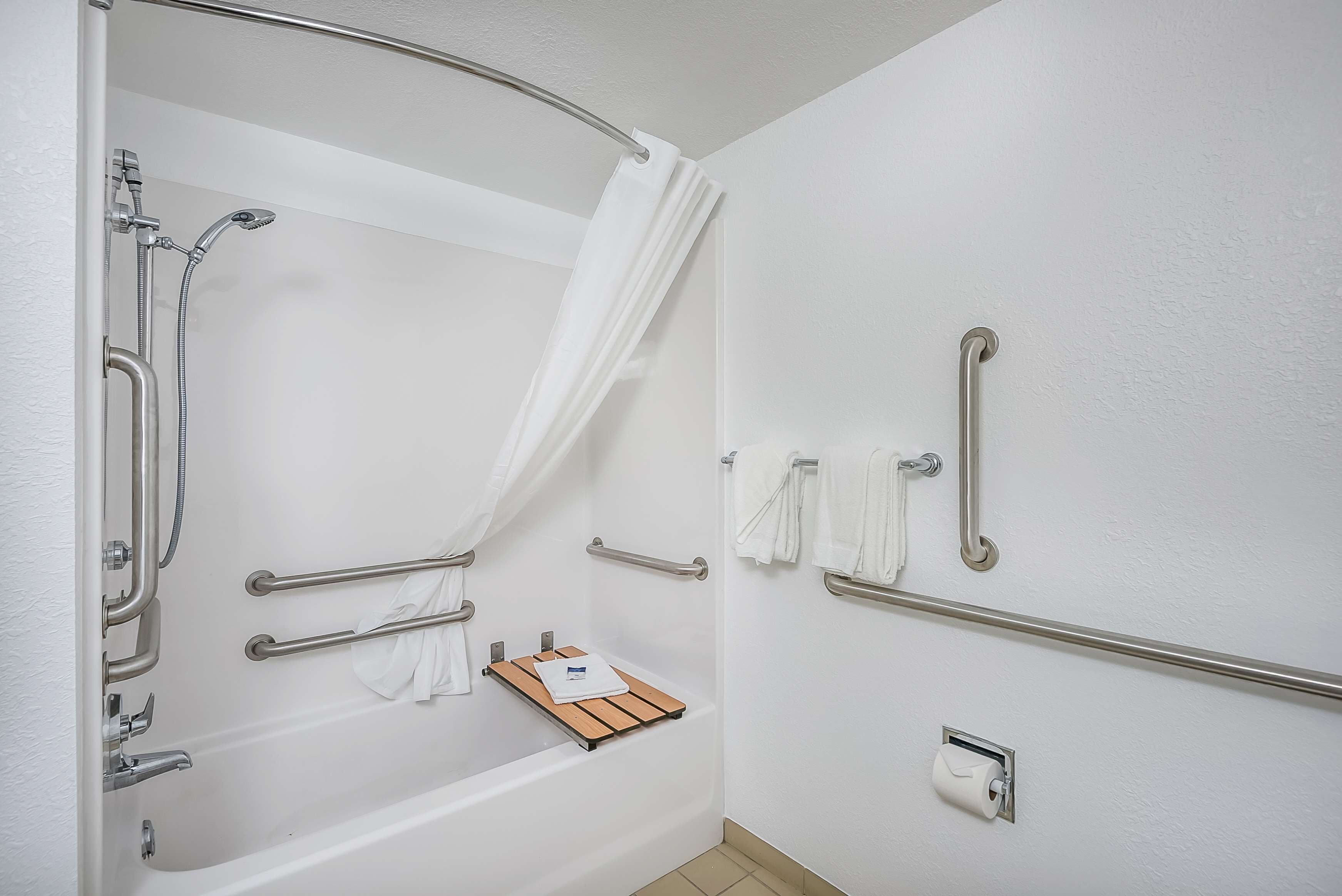 A modern bathroom with a bathtub, grab bars, a showerhead, and a towel rack.