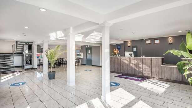 A modern hotel lobby with a reception desk, seating area, and a staircase. - Americas Best Value Inn East Peoria (East Peoria)