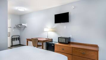 Habitación de hotel con cama, escritorio, silla, microondas, televisor, lámpara y cómoda.