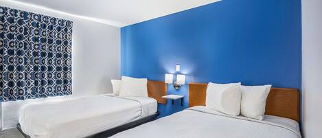 A hotel room with two beds, a blue accent wall, and a patterned curtain.