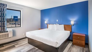 A hotel room with a large bed, two bedside tables, a window with curtains, and a view of the cityscape. - Americas Best Value Inn East Peoria (East Peoria)