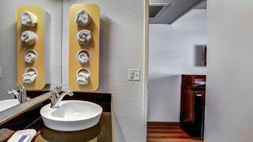 A bathroom with a sink, mirror, towel dispenser, and a microwave.