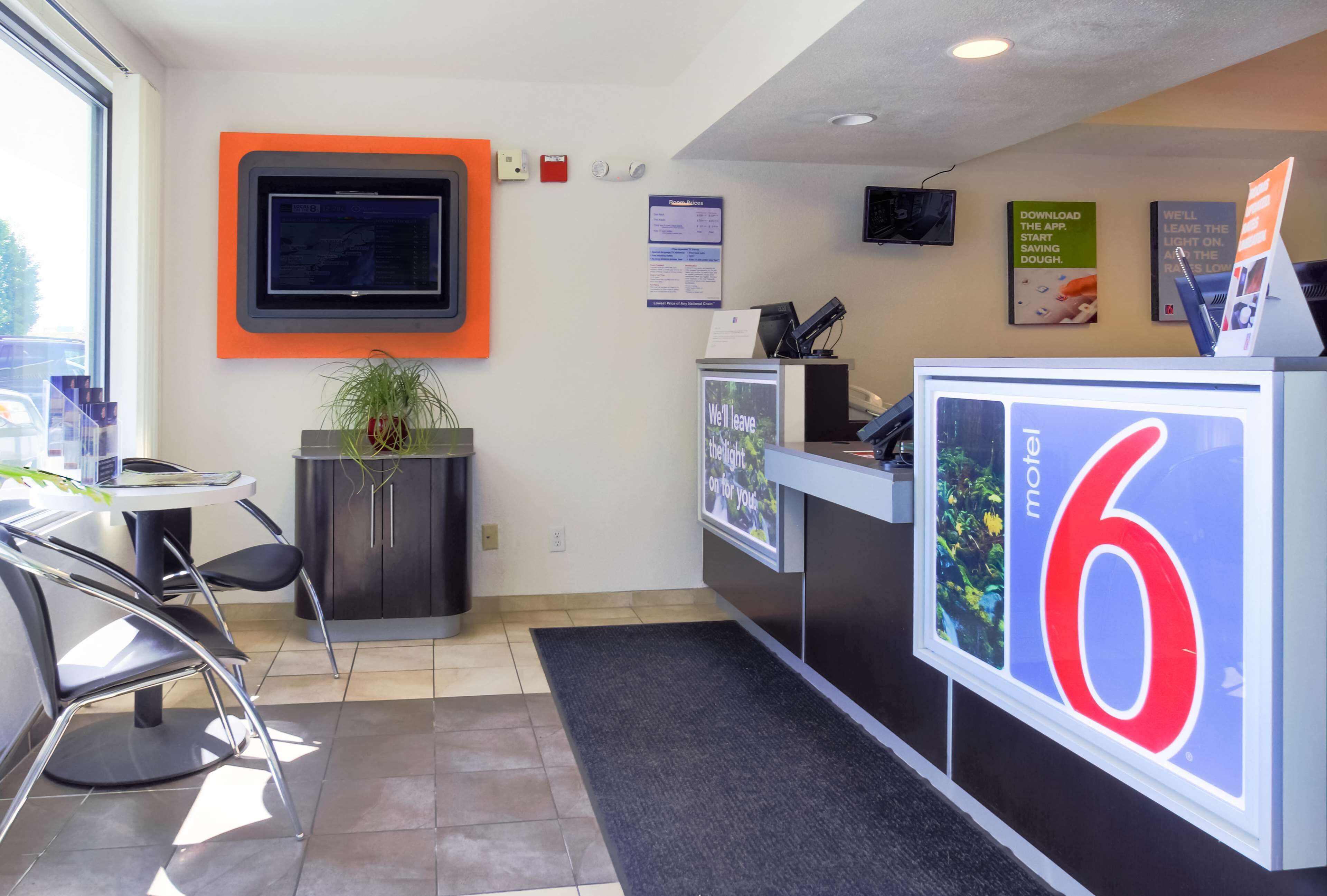 A reception area with a digital screen, a desk, chairs, a plant, and a sign indicating the number 6.