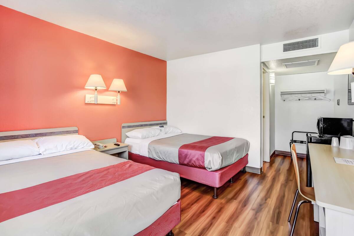 A hotel room with two beds, a desk, a chair, and a bathroom visible through an open door.