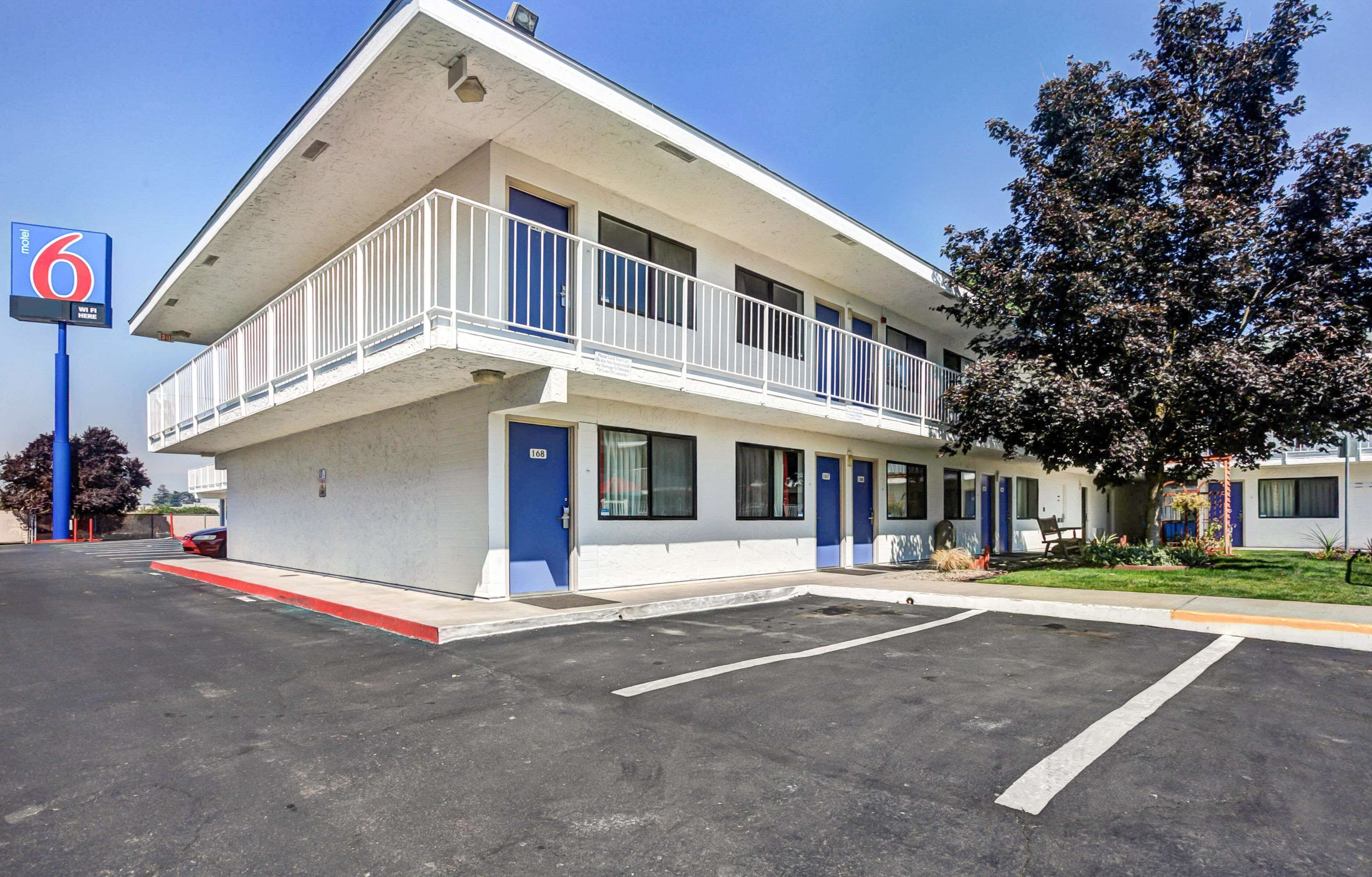 A motel with a two-story structure, a parking lot, and a tree in front.
