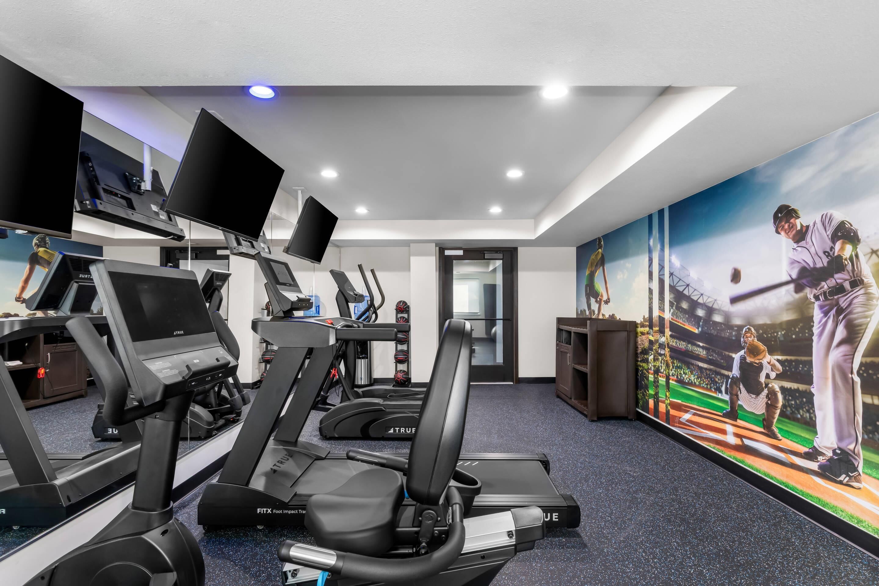Un gimnasio con cintas de correr, bicicletas estáticas y un gran mural de un jugador de béisbol.