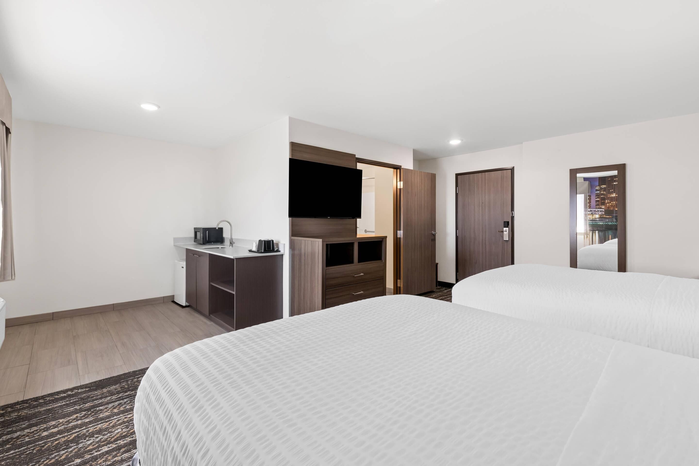 Une chambre d’hôtel avec deux lits, un bureau doté d’un téléviseur à écran plat, une armoire et un miroir.