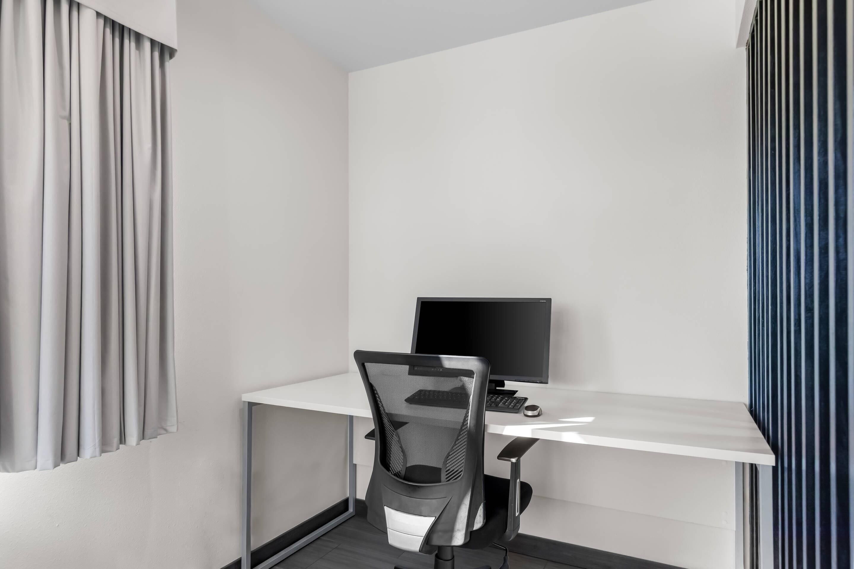 Un espacio de oficina moderno con un escritorio blanco, una silla de oficina de malla negra, un monitor de computadora y un teclado.