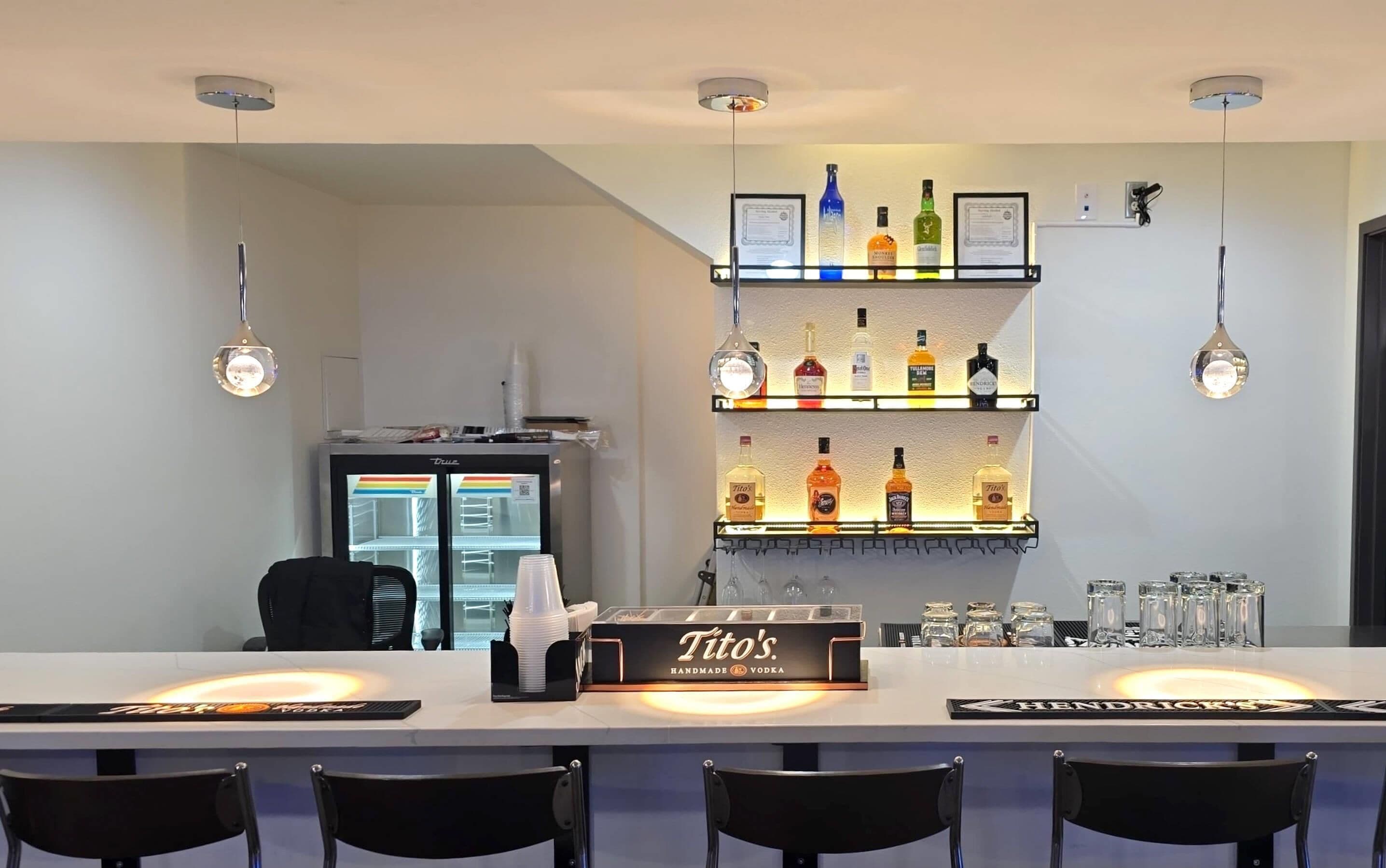 A bar area with a minibar, shelves of liquor bottles, and a branded vodka dispenser.