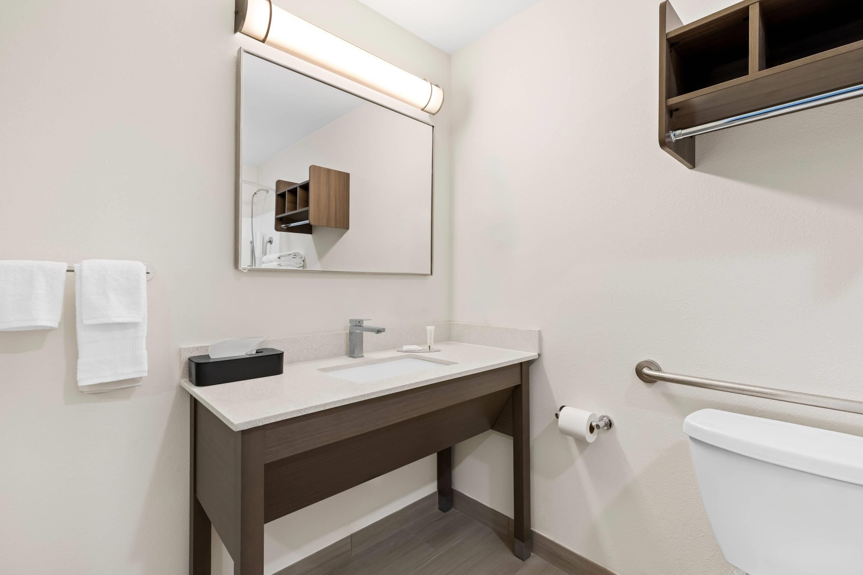 A modern bathroom with a sink, mirror, towel rack, and toilet.