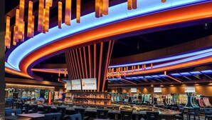 Un casino con múltiples mesas de juego y máquinas tragamonedas, iluminado por una iluminación vibrante.