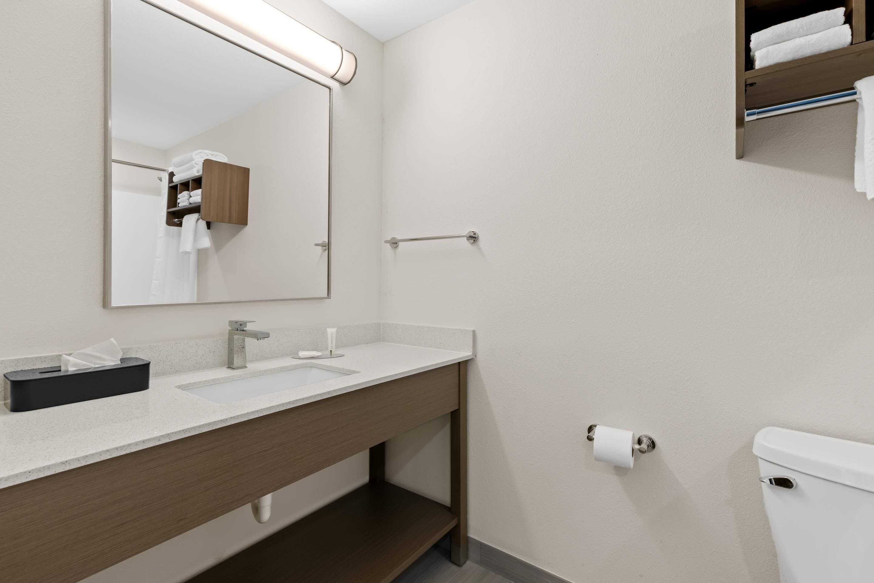 A modern bathroom with a large mirror, two sinks, a towel rack, and a toilet.