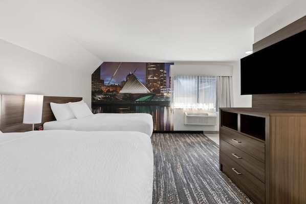 A hotel room with two beds, a large flat-screen TV, a desk, and a cityscape view.